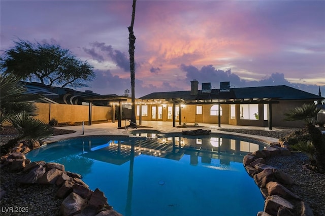 pool at dusk with a patio, fence, and a pool with connected hot tub