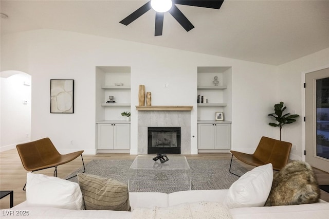 living area featuring built in shelves, ceiling fan, arched walkways, and vaulted ceiling