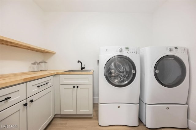 washroom featuring light wood finished floors, washer and clothes dryer, cabinet space, and a sink