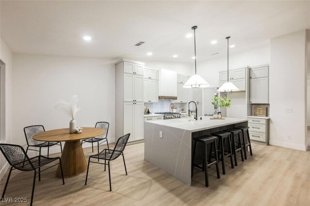 kitchen featuring light countertops, light wood-style floors, decorative backsplash, and a center island with sink