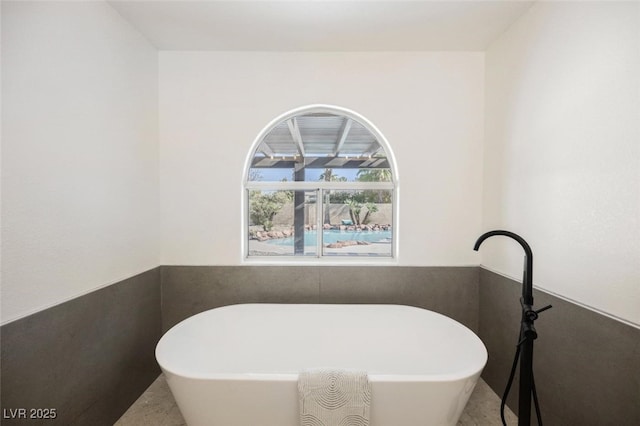 bathroom featuring a wainscoted wall and a soaking tub