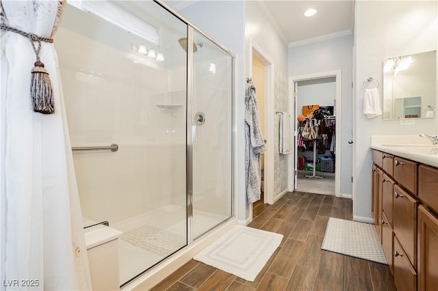 bathroom with a spacious closet, a shower stall, crown molding, wood finish floors, and vanity