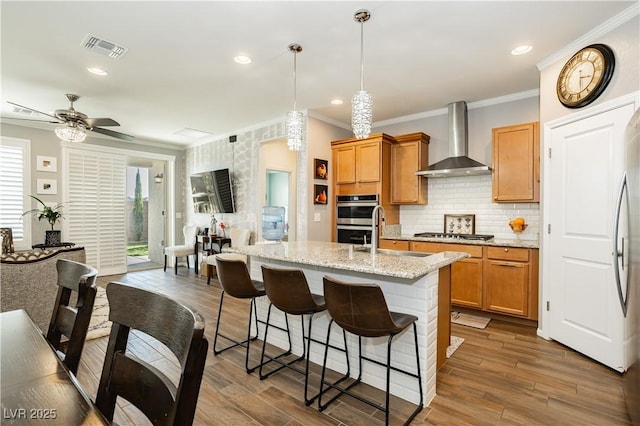 kitchen featuring visible vents, ornamental molding, wall chimney exhaust hood, and a sink