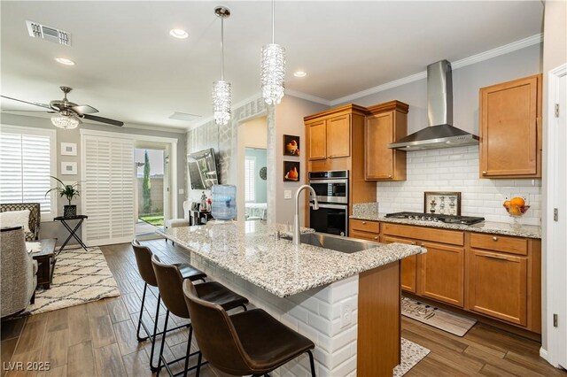9953 Fletcher Peak Ave, Las Vegas, NV 89178 - kitchen featuring wall chimney range hood, appliances with stainless steel finishes, ornamental molding, brown cabinets, and decorative backsplash