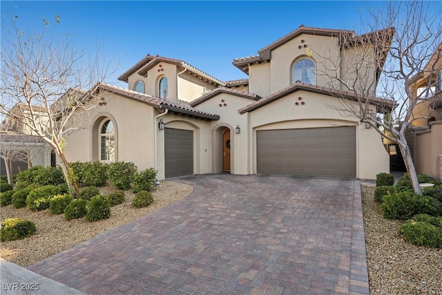 mediterranean / spanish-style home with stucco siding, decorative driveway, a tiled roof, and an attached garage
