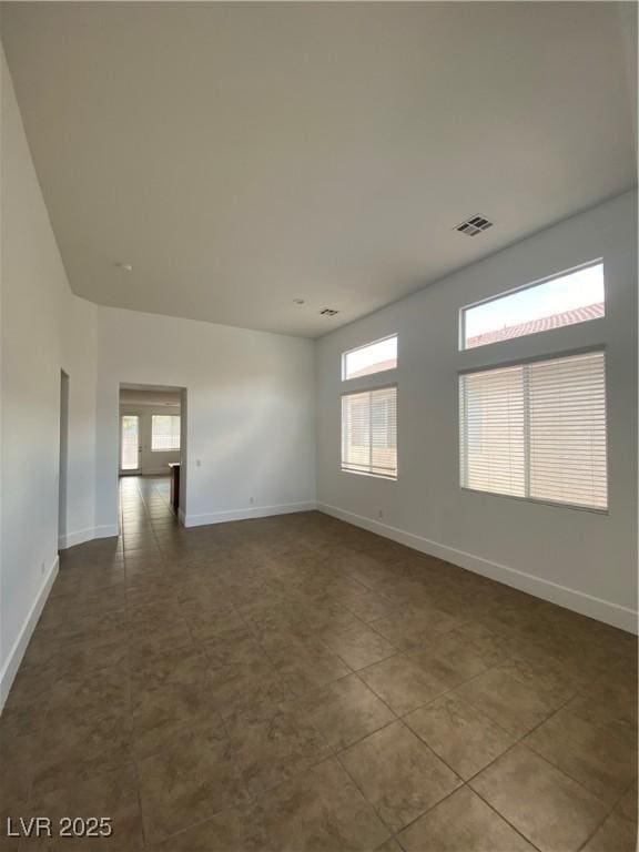 unfurnished room with baseboards, visible vents, a healthy amount of sunlight, and dark tile patterned floors