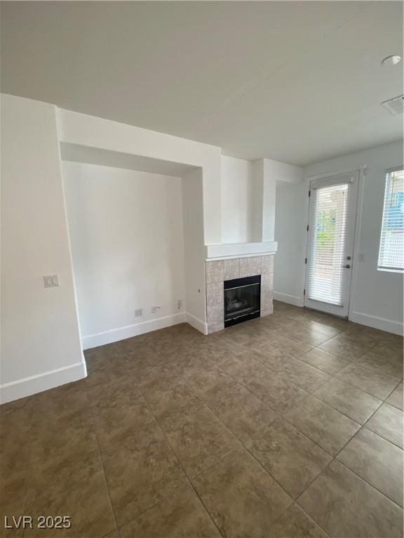 unfurnished living room featuring visible vents, a tiled fireplace, and baseboards