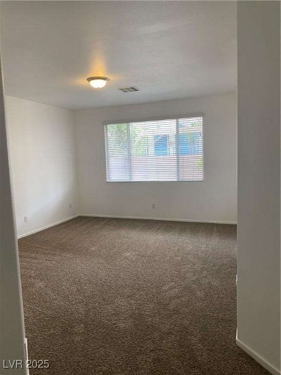 spare room featuring baseboards, visible vents, and dark carpet