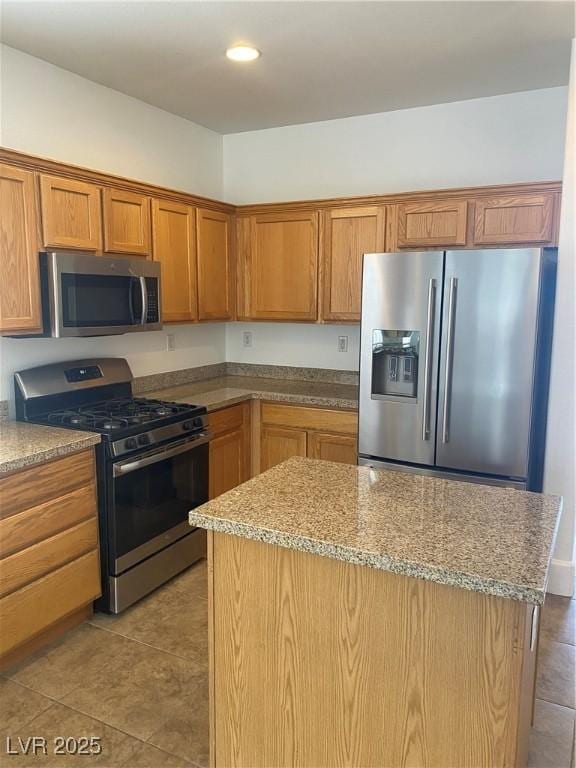 kitchen with tile patterned flooring, a kitchen island, stainless steel appliances, and light stone countertops