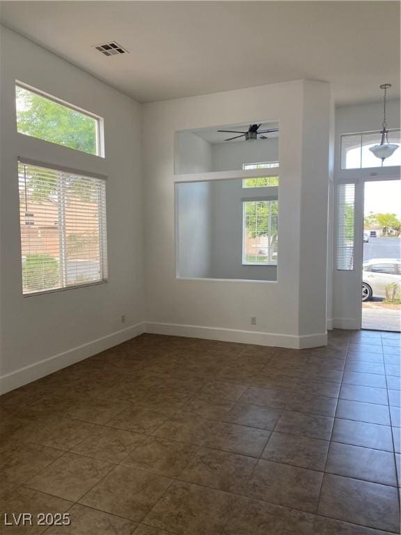 spare room with dark tile patterned flooring, a ceiling fan, visible vents, and baseboards