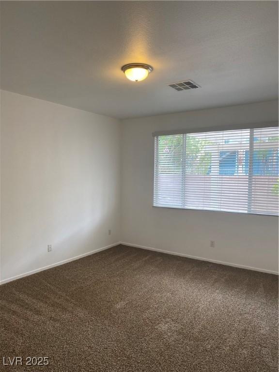 empty room featuring baseboards, visible vents, and dark carpet