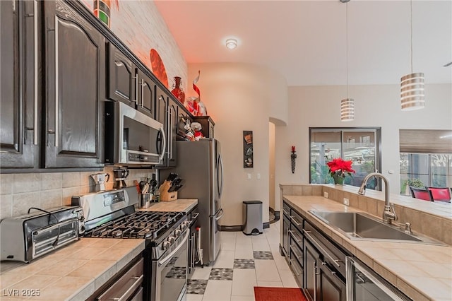 kitchen with a sink, stainless steel appliances, backsplash, tile countertops, and dark brown cabinets