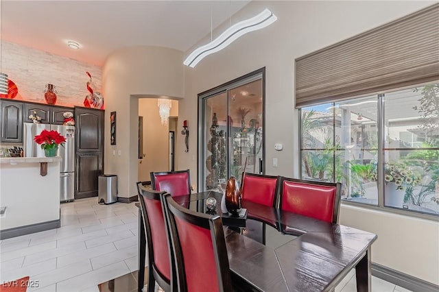 dining space featuring light tile patterned floors, arched walkways, and baseboards