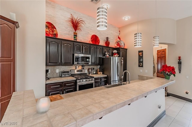 kitchen with light tile patterned floors, backsplash, a sink, stainless steel appliances, and hanging light fixtures
