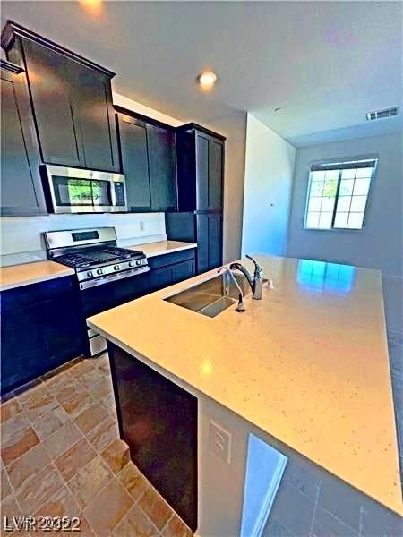 kitchen with a sink, appliances with stainless steel finishes, stone finish flooring, light countertops, and a kitchen island with sink