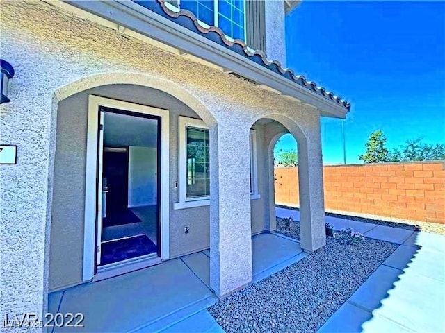 entrance to property featuring fence and stucco siding