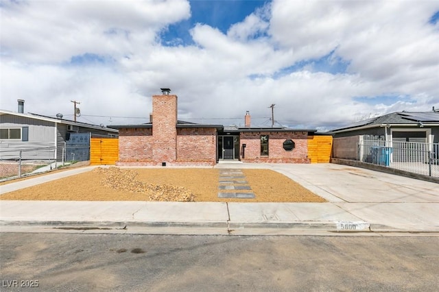 ranch-style home featuring solar panels, fence, a chimney, and brick siding