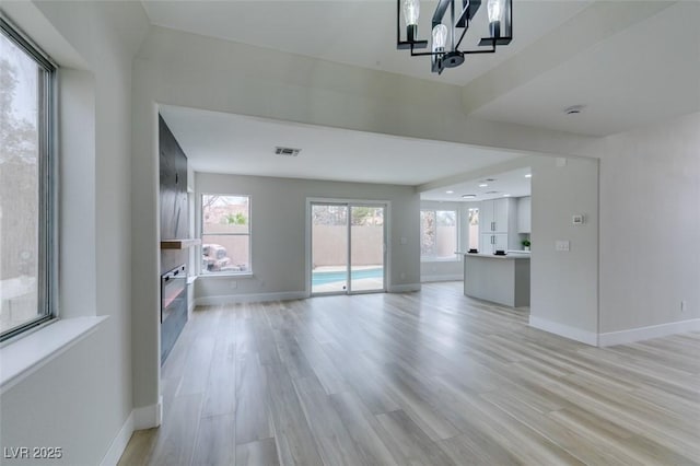 unfurnished living room with light wood-type flooring, visible vents, baseboards, and a glass covered fireplace