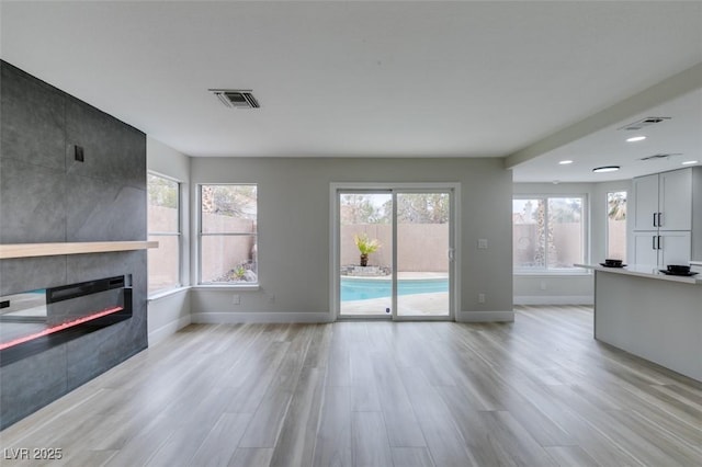 unfurnished living room featuring visible vents, a healthy amount of sunlight, baseboards, light wood finished floors, and a fireplace