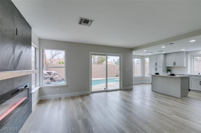 unfurnished living room with recessed lighting, light wood-style floors, a fireplace, visible vents, and baseboards