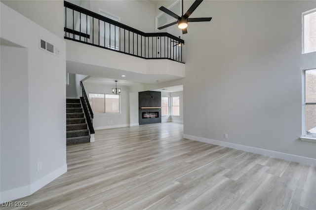 unfurnished living room featuring visible vents, ceiling fan, stairs, and a towering ceiling