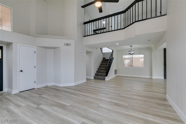 unfurnished living room with stairway, visible vents, baseboards, a towering ceiling, and ceiling fan with notable chandelier