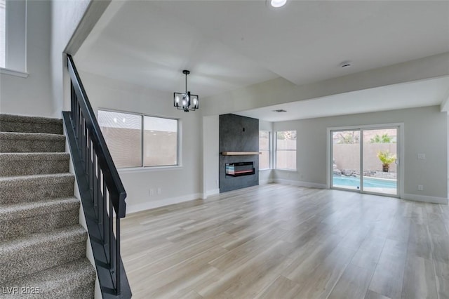 unfurnished living room featuring light wood-style floors, a notable chandelier, and stairs