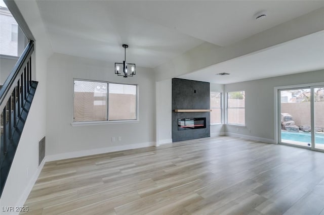 unfurnished living room featuring baseboards, a notable chandelier, a fireplace, and light wood finished floors