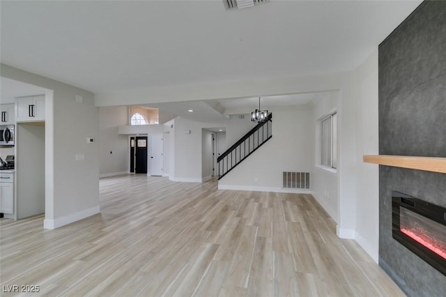 unfurnished living room with an inviting chandelier, stairs, light wood finished floors, a fireplace, and visible vents