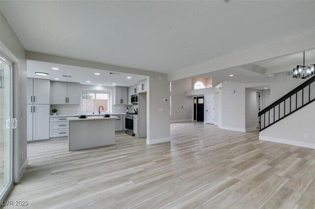 kitchen featuring light wood-style floors, appliances with stainless steel finishes, light countertops, a center island, and open floor plan