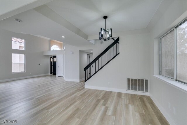 unfurnished living room featuring stairway, light wood-style floors, baseboards, visible vents, and a notable chandelier