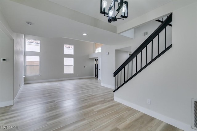 foyer entrance with visible vents, a chandelier, light wood finished floors, baseboards, and stairway