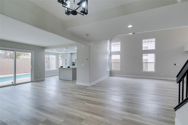 unfurnished living room with recessed lighting, an inviting chandelier, light wood-style flooring, baseboards, and stairway