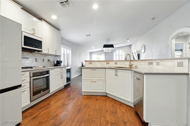 kitchen featuring dark wood-style flooring, white cabinets, a sink, appliances with stainless steel finishes, and backsplash