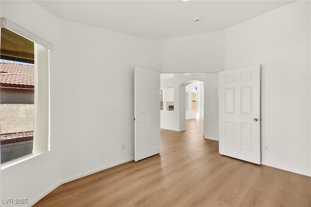 unfurnished room featuring light wood-style floors, arched walkways, and baseboards