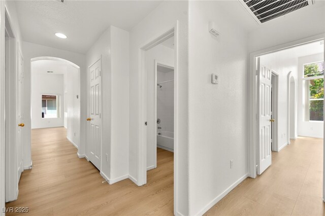 hallway with arched walkways, baseboards, light wood-type flooring, and visible vents