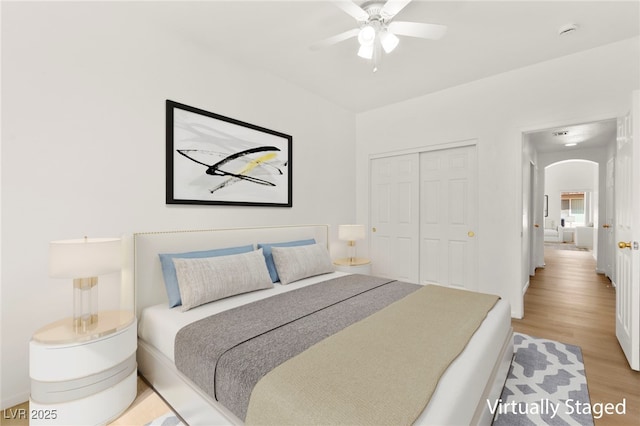 bedroom featuring arched walkways, ceiling fan, a closet, and light wood finished floors