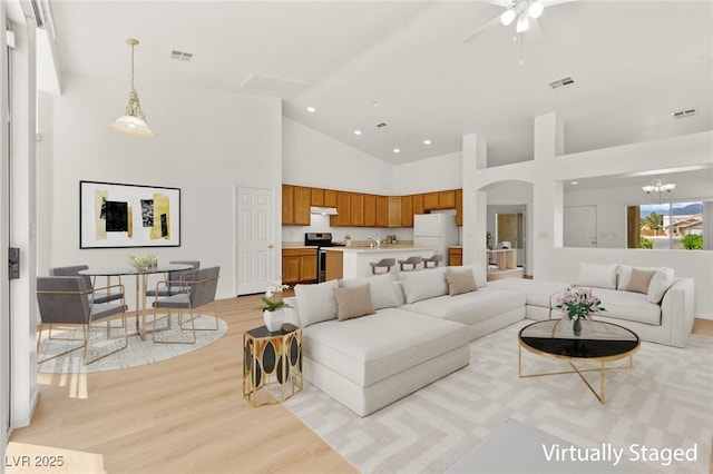 living room featuring high vaulted ceiling, ceiling fan with notable chandelier, light wood-style flooring, and visible vents