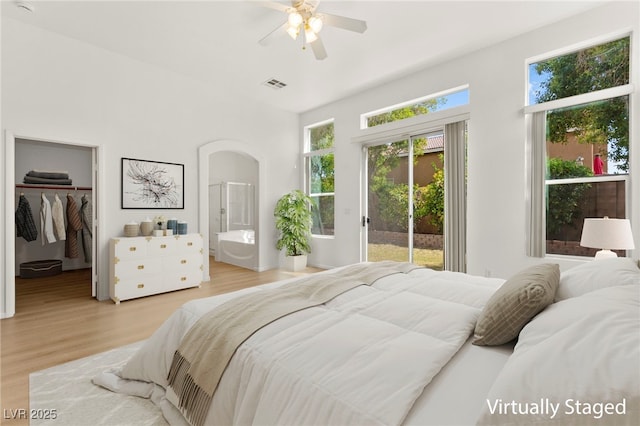 bedroom featuring arched walkways, access to exterior, wood finished floors, a spacious closet, and visible vents