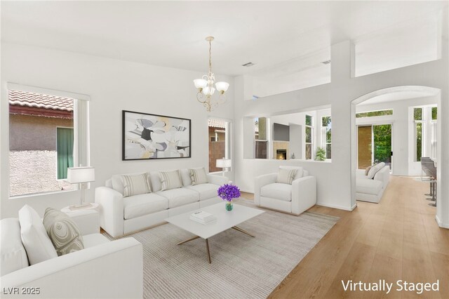 living room with an inviting chandelier, arched walkways, and light wood-style flooring