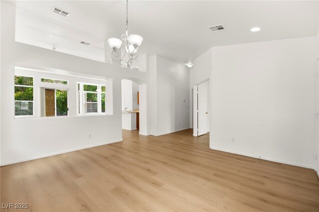 unfurnished living room featuring arched walkways, a notable chandelier, light wood finished floors, and visible vents