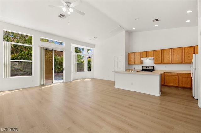 kitchen with stainless steel gas range oven, freestanding refrigerator, open floor plan, under cabinet range hood, and visible vents