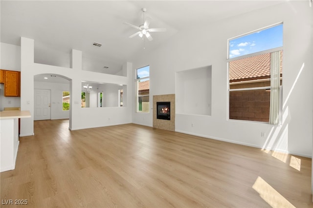 unfurnished living room with a fireplace, high vaulted ceiling, ceiling fan with notable chandelier, light wood-type flooring, and visible vents