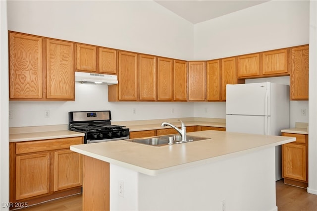 kitchen with freestanding refrigerator, stainless steel gas range oven, light wood-type flooring, light countertops, and under cabinet range hood