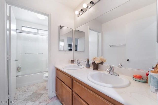 bathroom featuring double vanity, toilet, combined bath / shower with glass door, and a sink