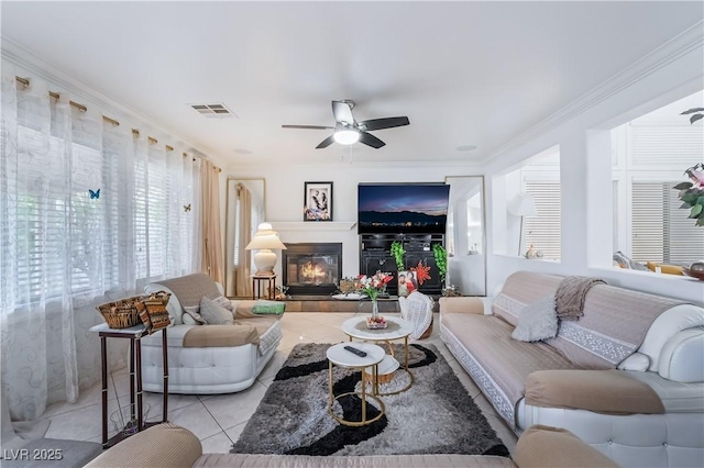 tiled living room with a glass covered fireplace, crown molding, ceiling fan, and visible vents