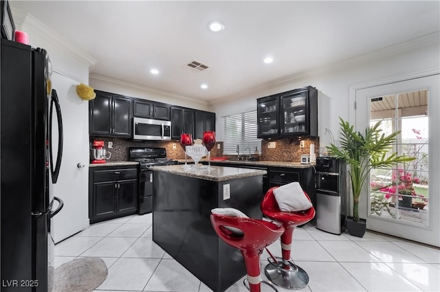 kitchen featuring dark cabinets, freestanding refrigerator, stainless steel microwave, and range with gas cooktop