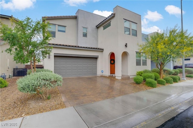 mediterranean / spanish house with an attached garage, a tiled roof, stucco siding, and decorative driveway