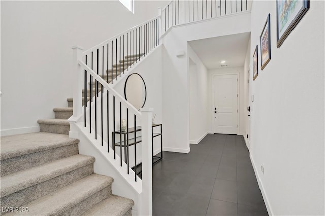 stairs with tile patterned flooring, baseboards, and a high ceiling