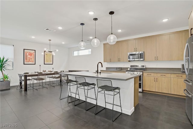 kitchen featuring light brown cabinets, a breakfast bar, visible vents, a sink, and stainless steel appliances